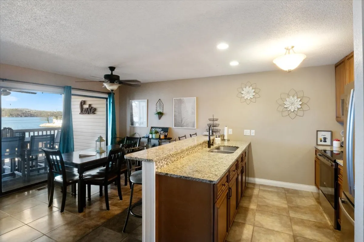 An inviting dining area set adjacent to a granite-countered kitchen, with a dining table perfectly positioned beside a sliding glass door that opens to stunning lake views. Decorative wall art and natural light enhance the welcoming, relaxed vibe, ideal for family meals or gatherings.