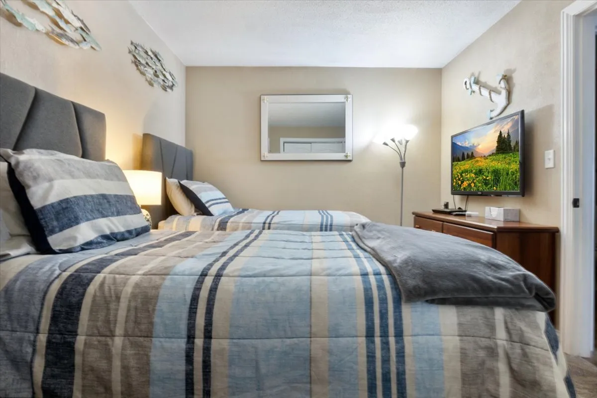 A playful and spacious bunk room equipped with two beds featuring striped bedding, cheerful wall art, a large mirror, and a TV on a wooden console. The vibrant decor and ample space capture the room’s family-friendly and adventurous spirit.
