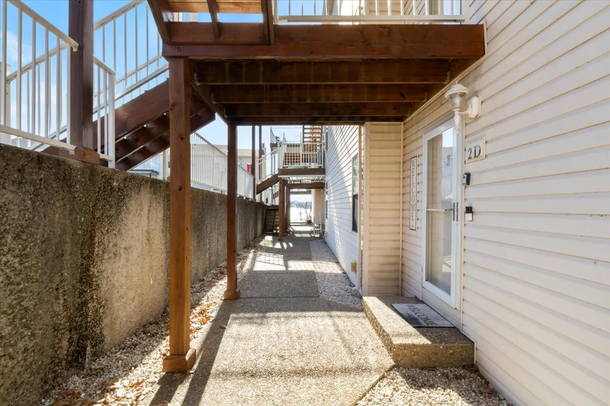 This image features a wooden staircase and entrance walkway framed by greenery, leading to an inviting doorway. The casual outdoor setting hints at easy access to nature and opportunities for strolls or friendly encounters around the property.