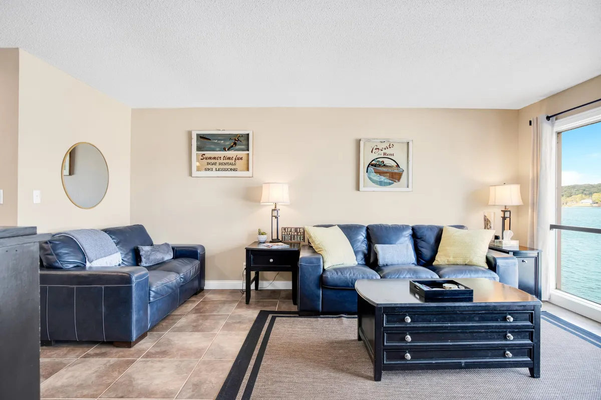 A modern living area featuring blue leather sofas, a coffee table, and large windows offering water views. Accented by decorative wall art, this space exudes comfort and invites guests to relax or socialize while soaking in the calming scenery.