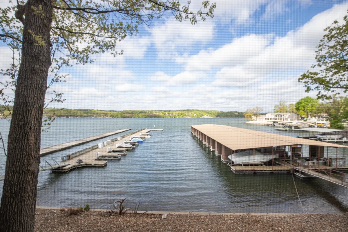 A sweeping view of the lakefront showcasing docks, boats moored in the marina, and lush trees surrounding the water. The tranquil water reflects the sky, and the area is clearly set up for boating and lakeside activities.