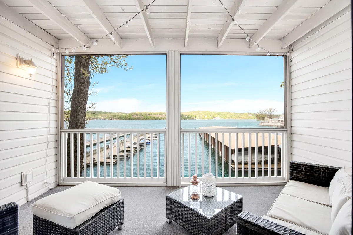 An exterior view of a balcony with inviting outdoor seating and a decorative table overlooking a stunning lake view. The ambiance is serene, perfect for sunset reflections, starlit evenings, or simply soaking in the natural beauty that surrounds the property.